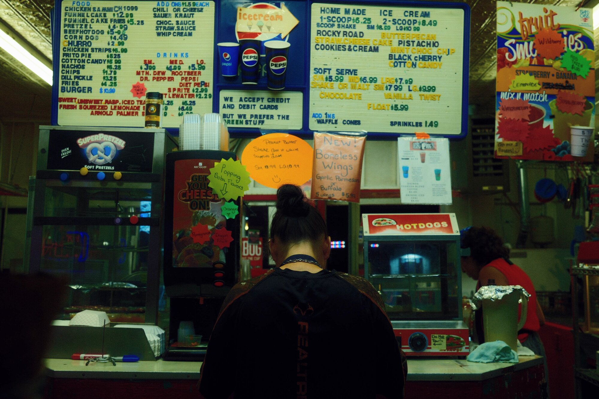 Concession worker beneath hand-lettered menu boards and Pepsi signs