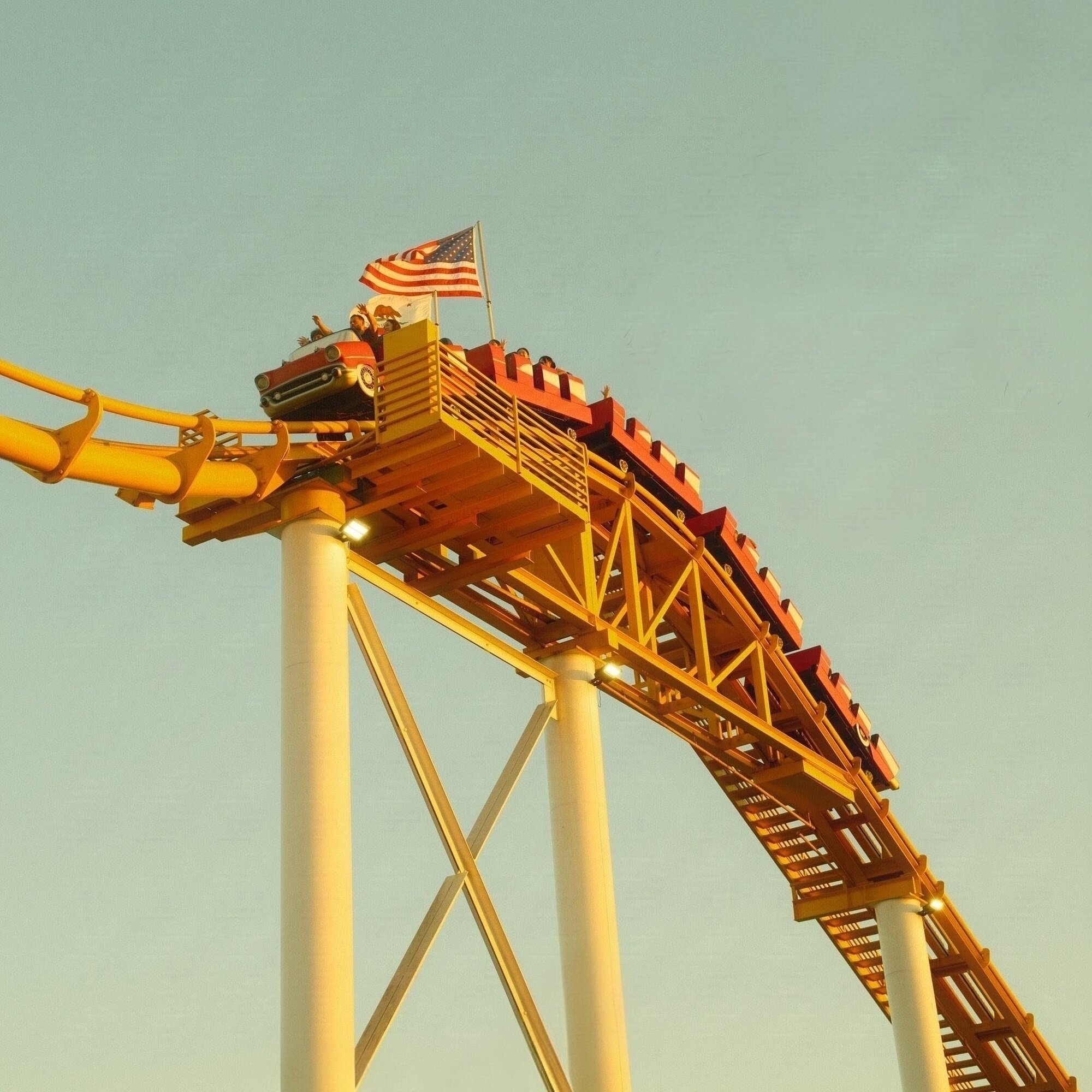 Vintage-car roller coaster cresting a golden track under American flag